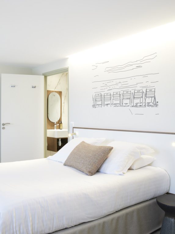 Chambre de l’hôtel du Pin à Nice avec lit king size, une illustration au mur de la promenade des anglais, vue sur salle de bain et dressing