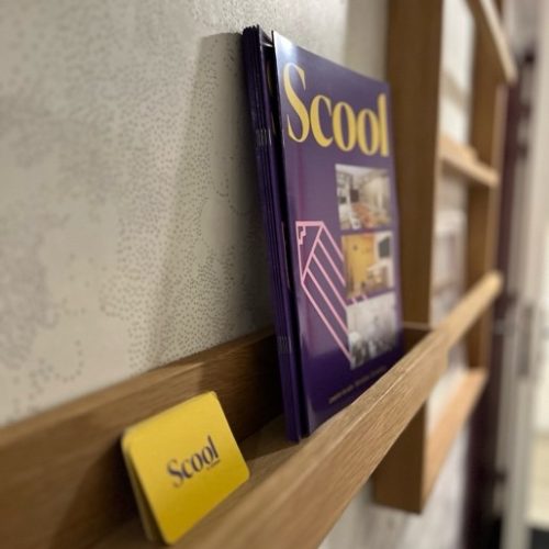 Zoom sur des brochures Scool adossées au mur avec des cartes de visite jaunes Scool