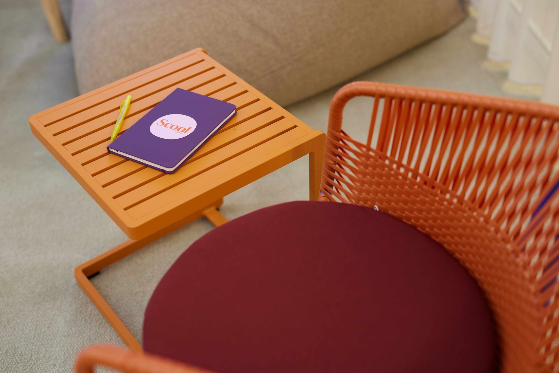 Table orange avec un carnet violet avec inscription Scool et un stylo jaune et le siège orange et rouge